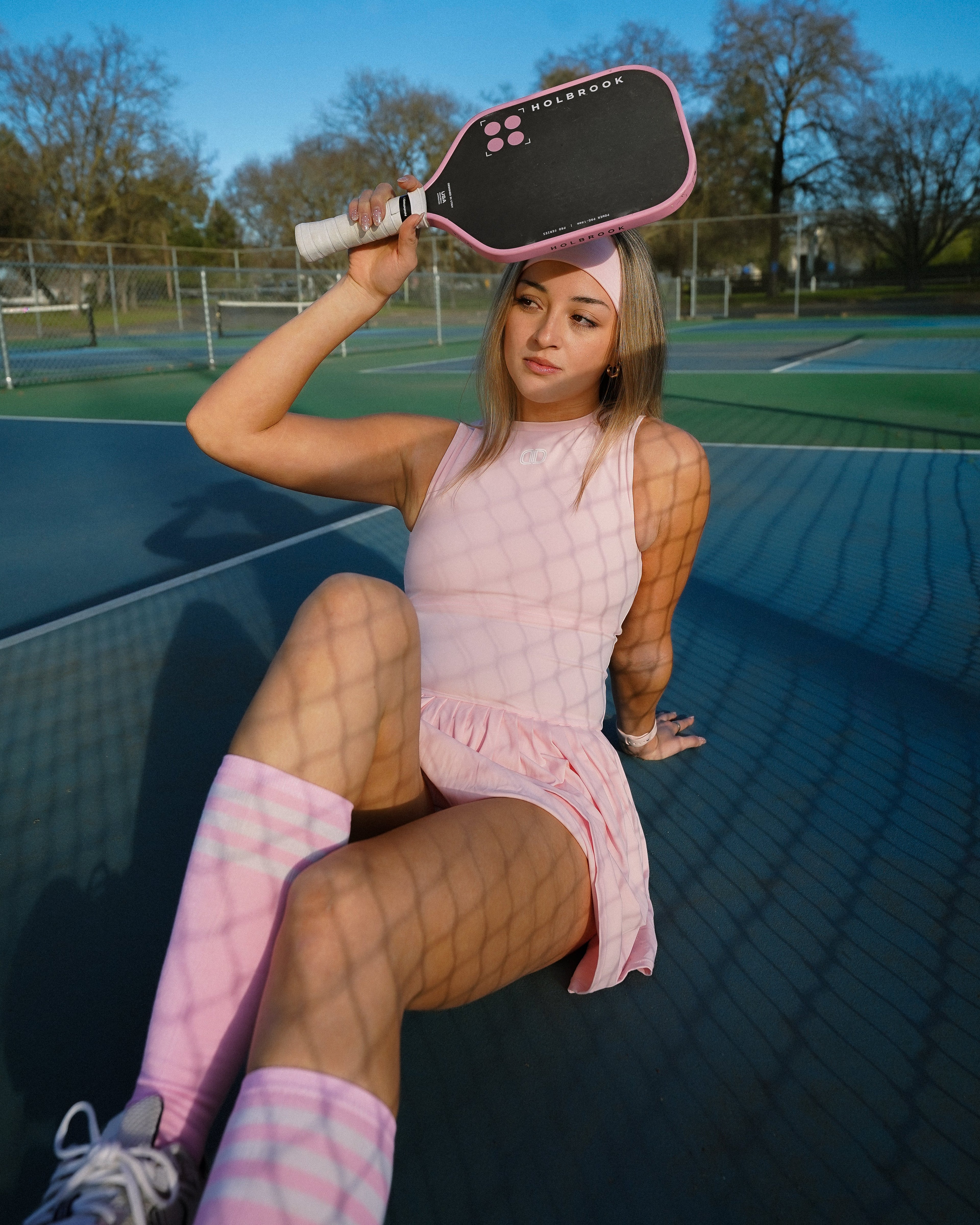 women wearing pink pickleball dress sitting on the court in the shadows of the net